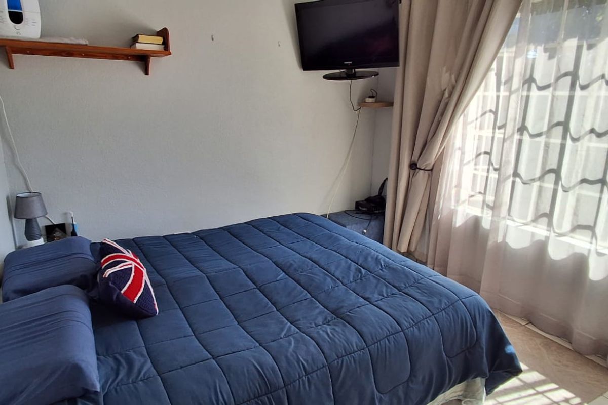 A functional bedroom featuring tiled flooring and large windows with curtain rails, providing natural light and a comfortable living space.