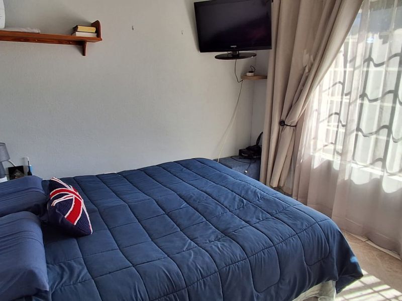 A functional bedroom featuring tiled flooring and large windows with curtain rails, providing natural light and a comfortable living space.