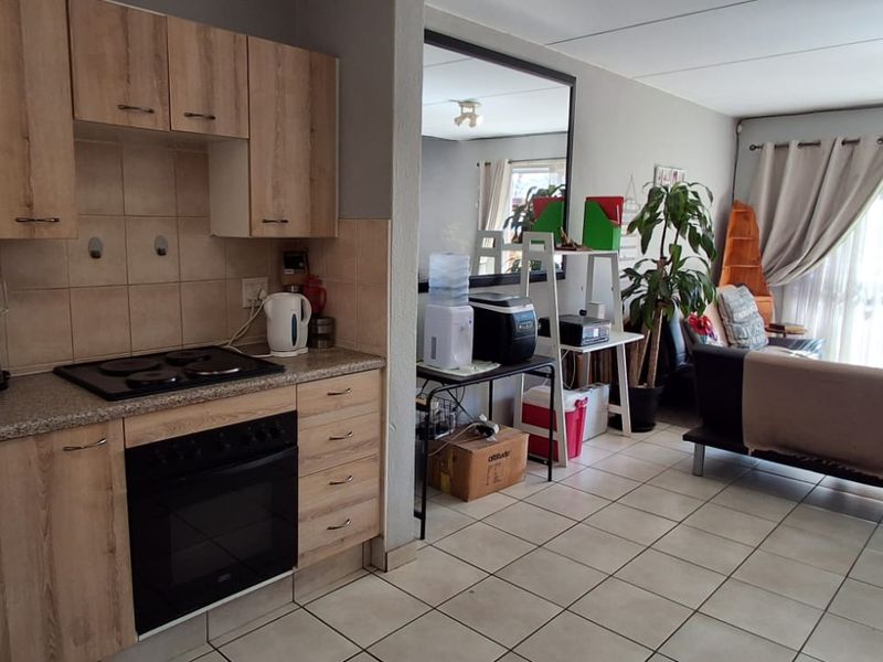Open-plan kitchen and living area featuring tiled floors, wood-look cabinetry, built-in oven and hob, and direct access to an outdoor patio through sliding doors.