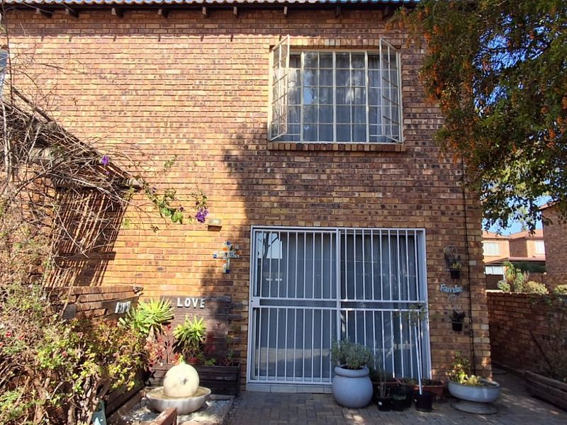 Rear exterior view of a face brick townhouse featuring a paved patio area, security-fitted sliding doors, and upper-level casement windows.