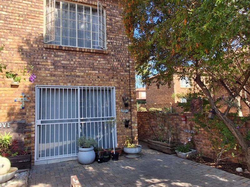 Rear exterior view of a face brick townhouse featuring a paved patio area, security gate, and established garden boundary wall.