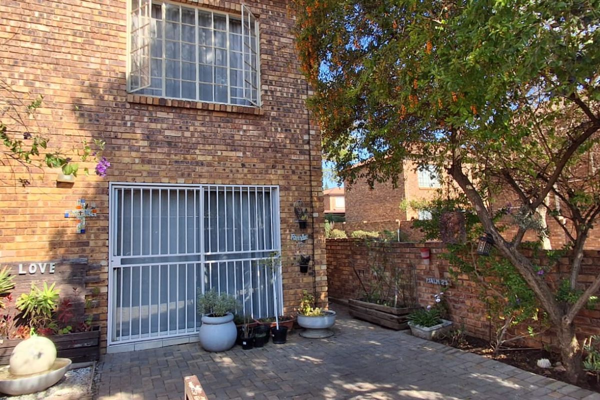 Rear exterior view of a face brick townhouse featuring a paved patio area, security gate, and established garden boundary wall.