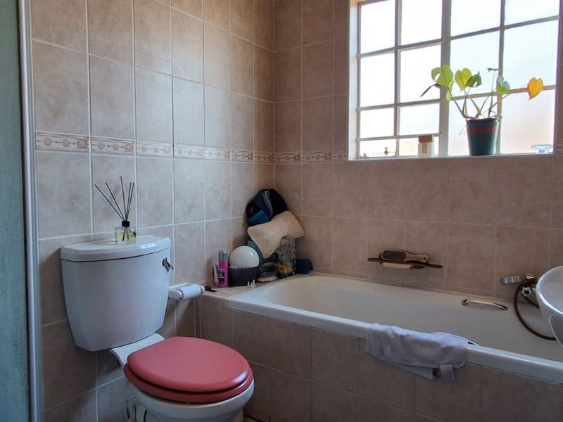 A functional bathroom featuring a built-in bathtub, shower enclosure, pedestal basin, and toilet, finished with neutral wall and floor tiling.