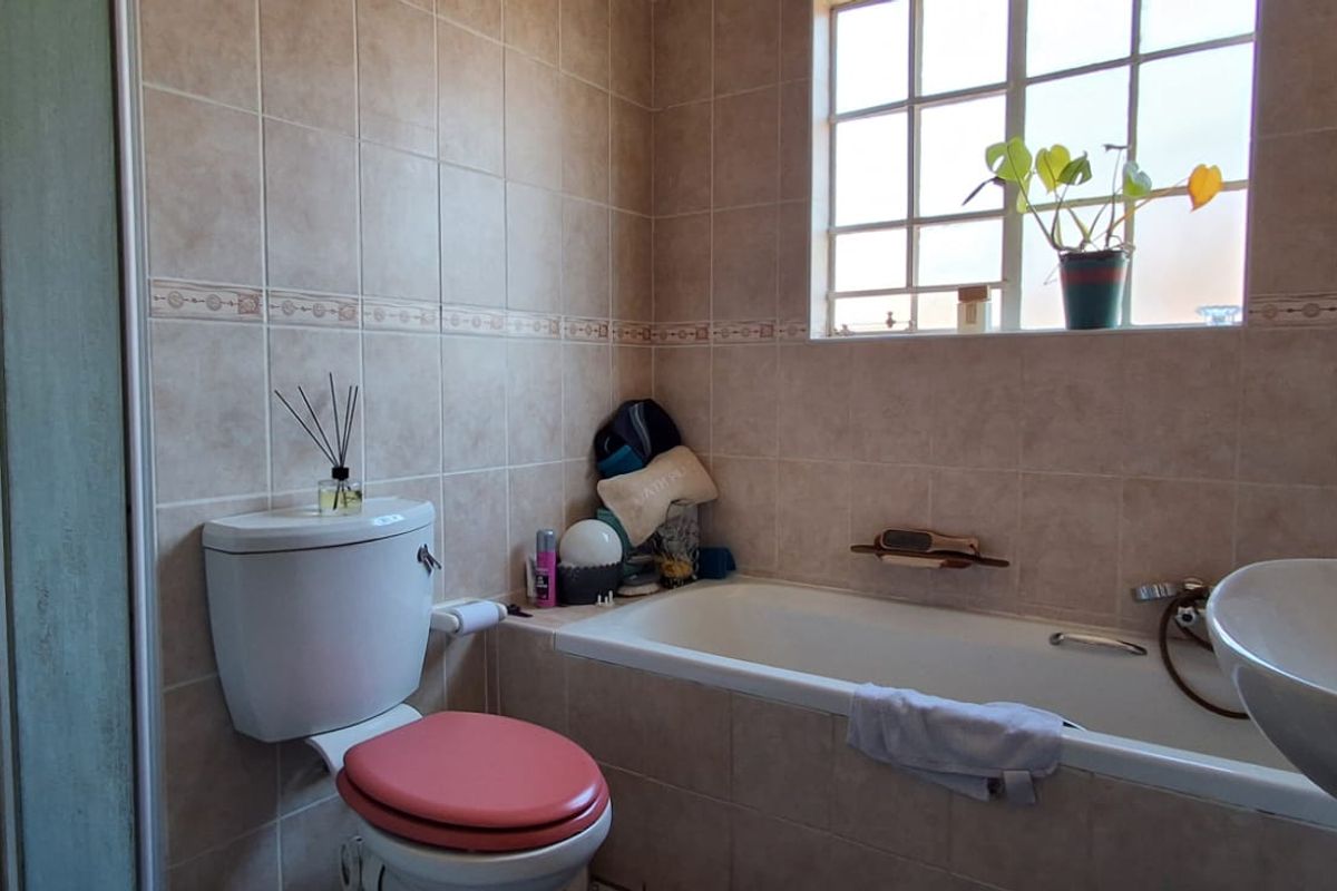A functional bathroom featuring a built-in bathtub, shower enclosure, pedestal basin, and toilet, finished with neutral wall and floor tiling.