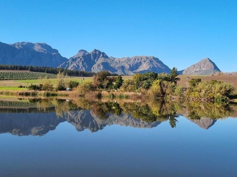 A scenic view of a tranquil dam reflecting the surrounding mountain range and expansive farmland on this picturesque farm property.