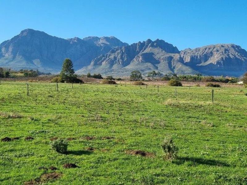 Expansive green pasture land featuring wire fencing with scenic mountain range views in the background.