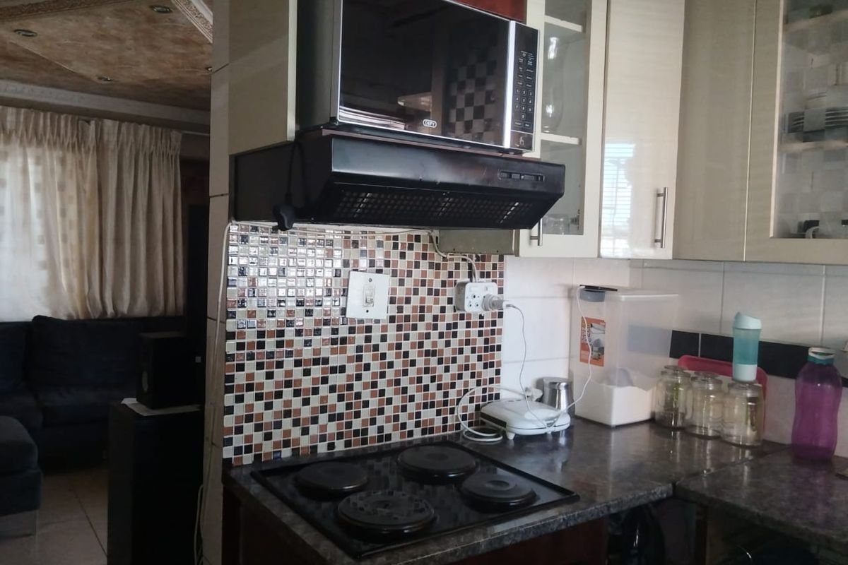 A functional kitchen area featuring a mosaic tile backsplash, built-in cabinetry, an electric hob, and an integrated extractor fan with a microwave.
