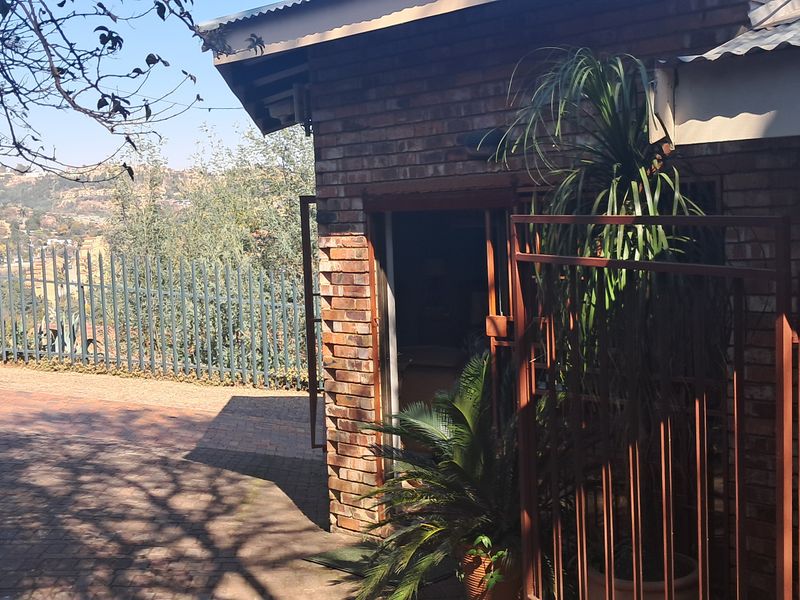 Rear exterior view of a face brick cottage featuring a paved area, metal security gate, and perimeter fencing with scenic hillside views.