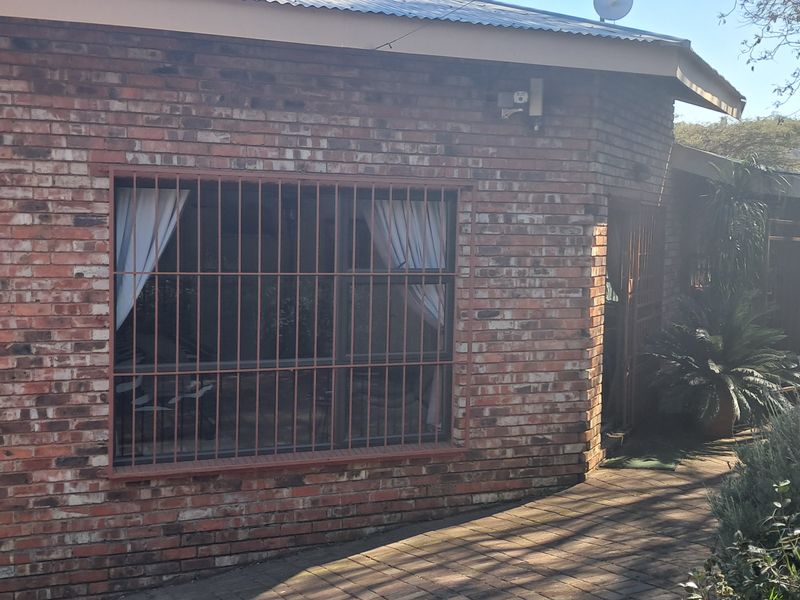 A cottage-style home featuring a classic face brick facade, secure window bars, and a paved driveway entrance.