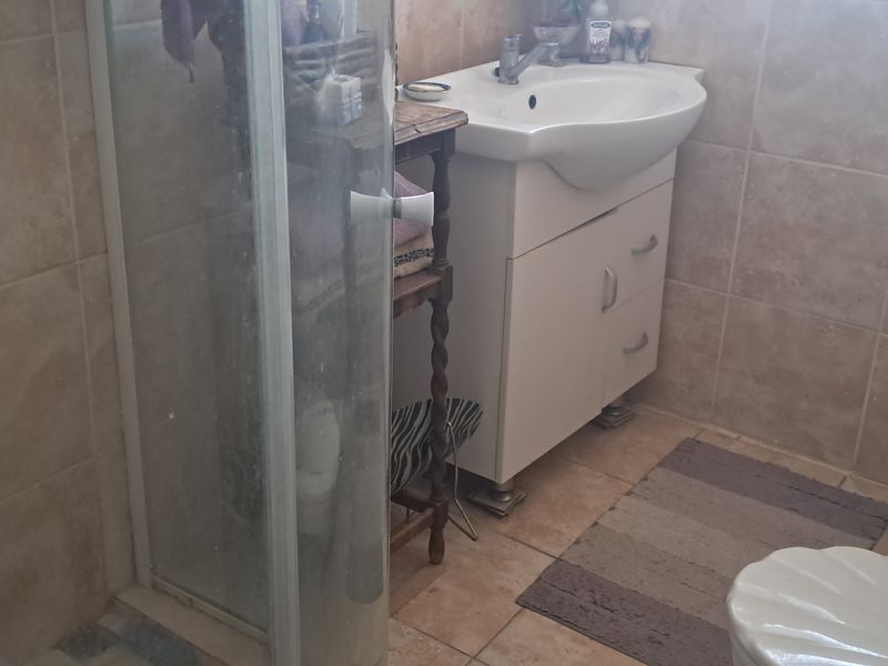 A functional bathroom featuring a shower enclosure, vanity basin, and neutral wall and floor tiling.