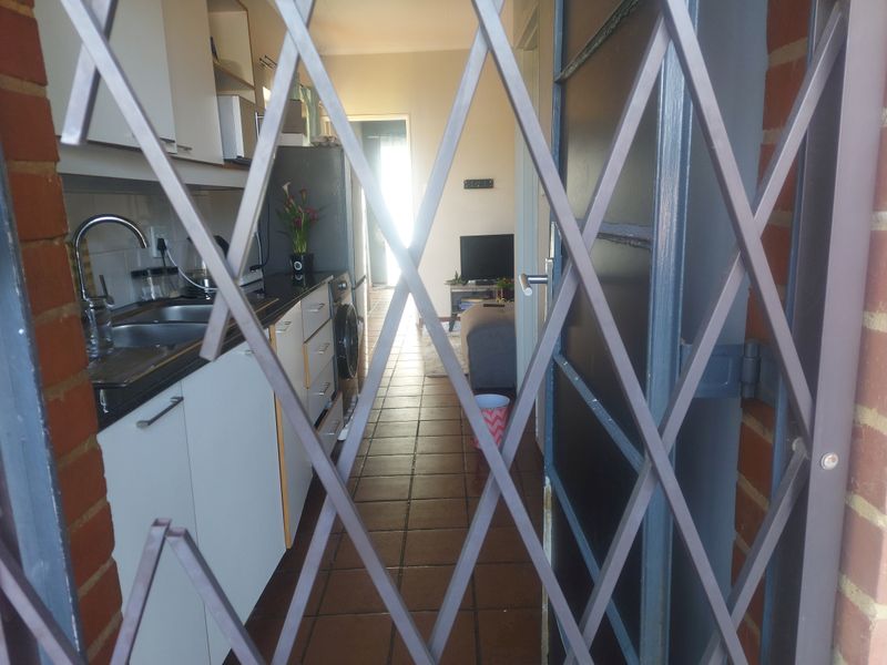 An open-plan kitchen and living area featuring tiled flooring and built-in cabinetry, viewed through a security gate.