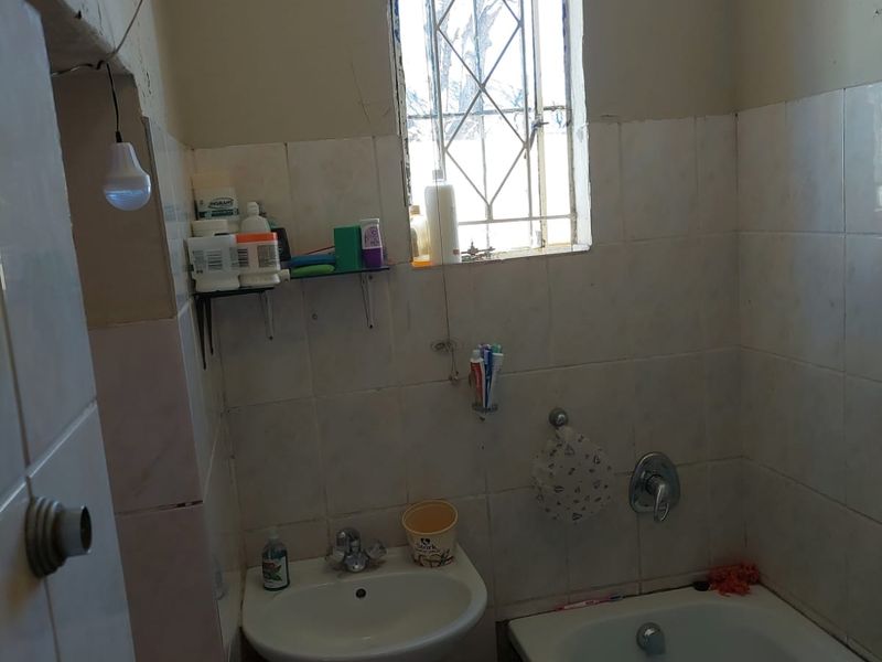 A compact bathroom featuring a pedestal basin, bathtub, and tiled walls, currently requiring significant maintenance and cosmetic updates to improve its condition.