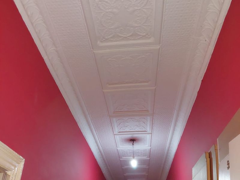 A hallway featuring a decorative pressed metal ceiling with coving and a central pendant light fixture.