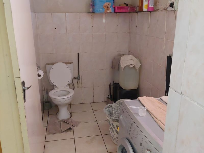 A functional laundry and bathroom space featuring tiled walls and flooring, equipped with a toilet and plumbing connections for laundry appliances.