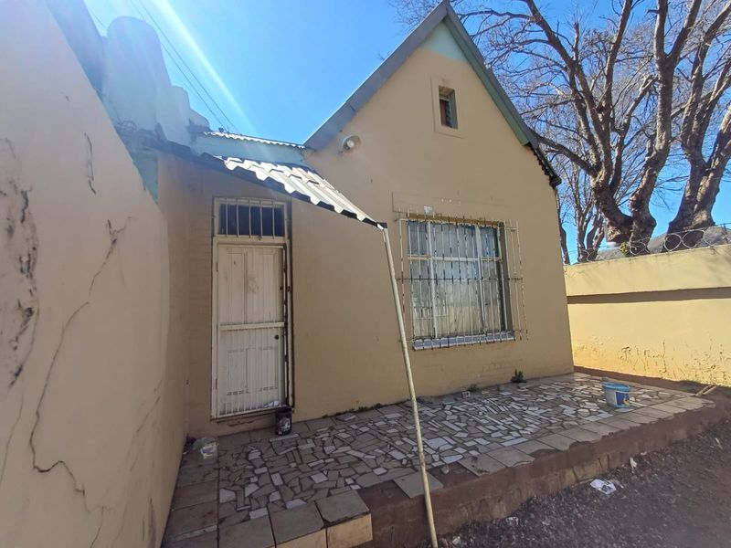 Front exterior view of a townhouse featuring a tiled patio area, security bars on windows, and a perimeter wall with razor wire.