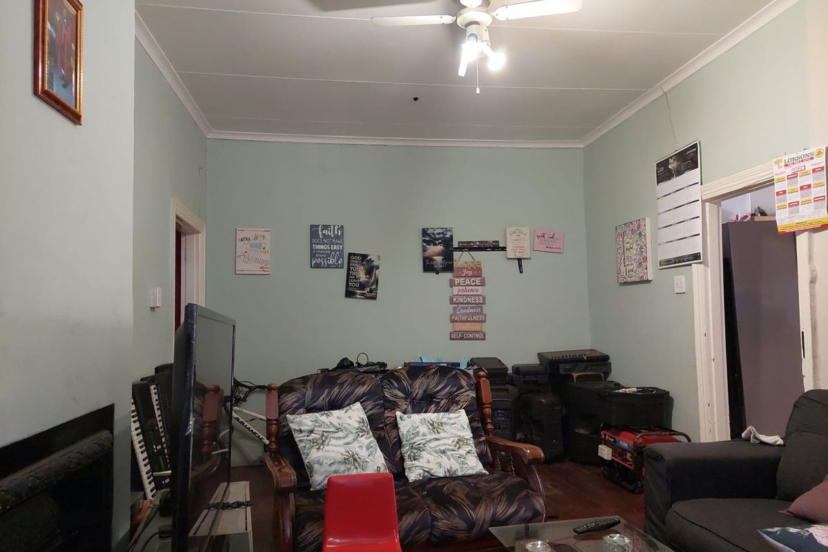 A living room featuring a fireplace, ceiling fan, and coving, currently showing signs of wear including visible wall cracks.
