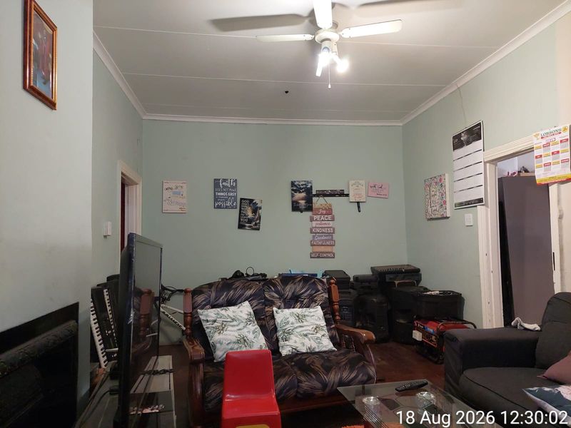 A living room featuring a fireplace, ceiling fan, and coving, currently showing signs of wear including visible wall cracks.