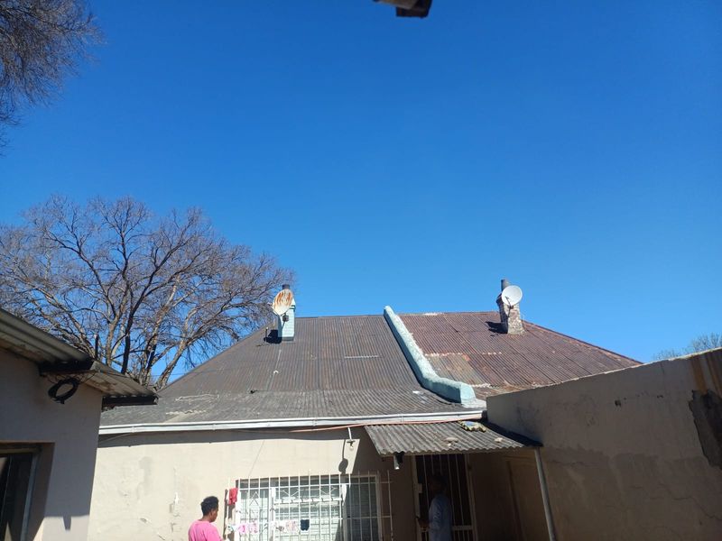 Rear view of the townhouse showing a corrugated iron roof with visible signs of corrosion and exterior walls requiring maintenance.
