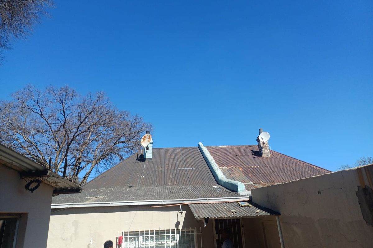 Rear view of the townhouse showing a corrugated iron roof with visible signs of corrosion and exterior walls requiring maintenance.