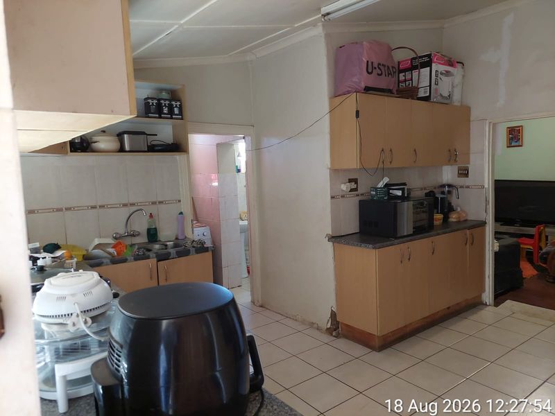 A functional kitchen featuring laminate cabinetry, tiled flooring, and a tiled backsplash, requiring cosmetic updates to improve its overall condition and aesthetic appeal.