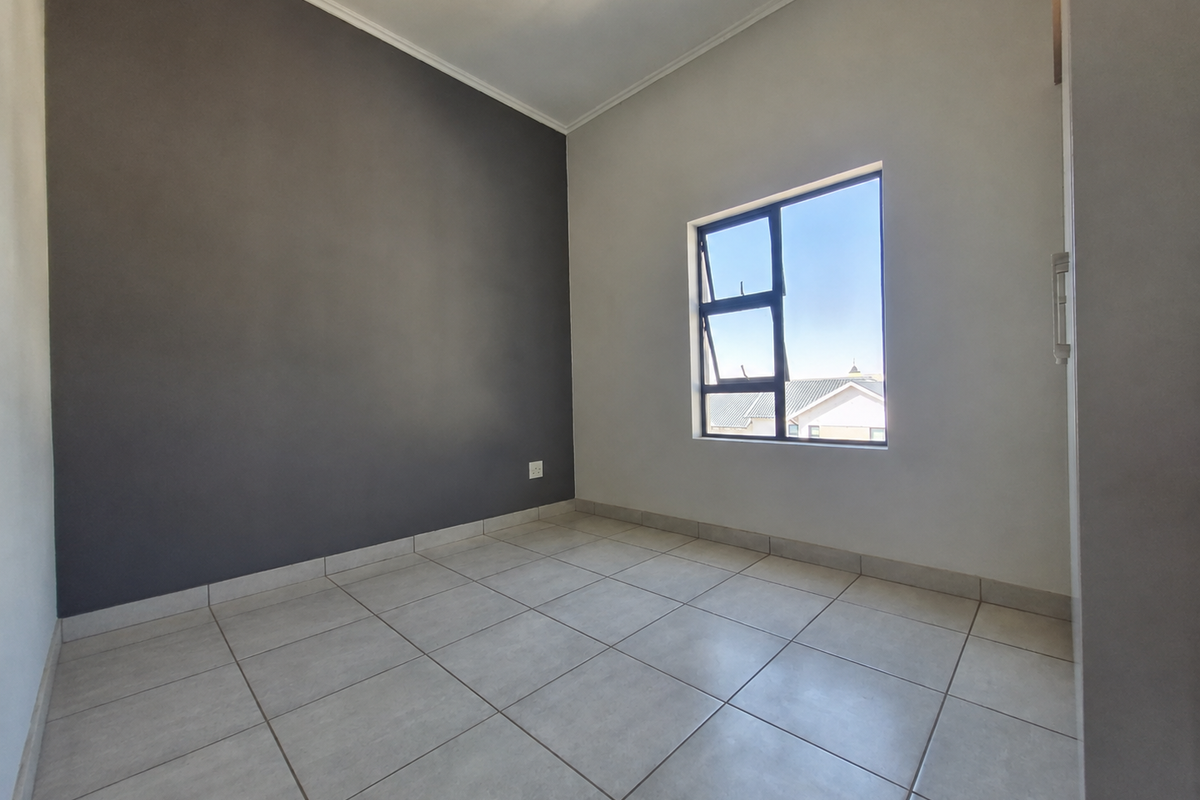 A bright, empty bedroom featuring neutral tiled flooring, a dark accent wall, and a casement window providing natural light.