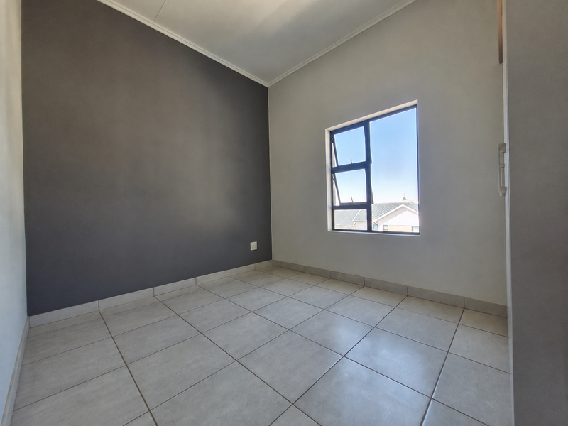 A bright, empty bedroom featuring neutral tiled flooring, a dark accent wall, and a casement window providing natural light.
