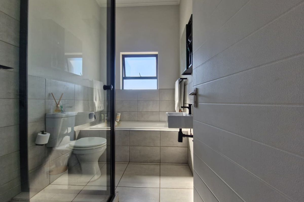 Modern bathroom featuring a glass-enclosed shower, a built-in bathtub, a wall-mounted basin, and neutral floor-to-ceiling tiling.