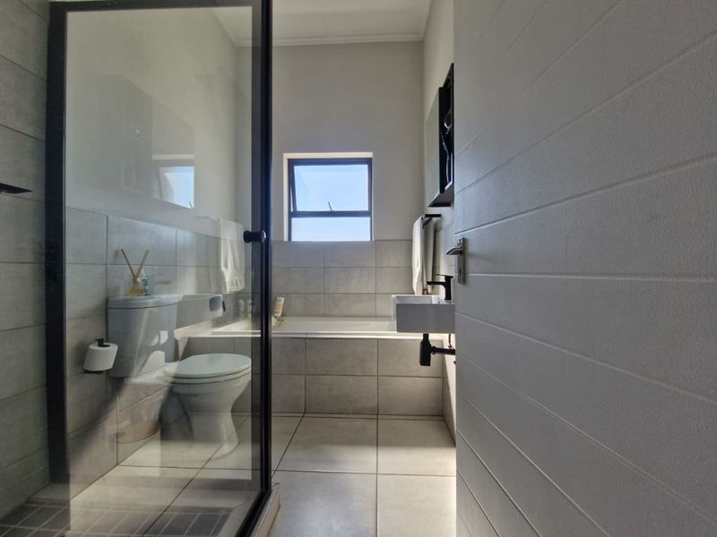 Modern bathroom featuring a glass-enclosed shower, a built-in bathtub, a wall-mounted basin, and neutral floor-to-ceiling tiling.