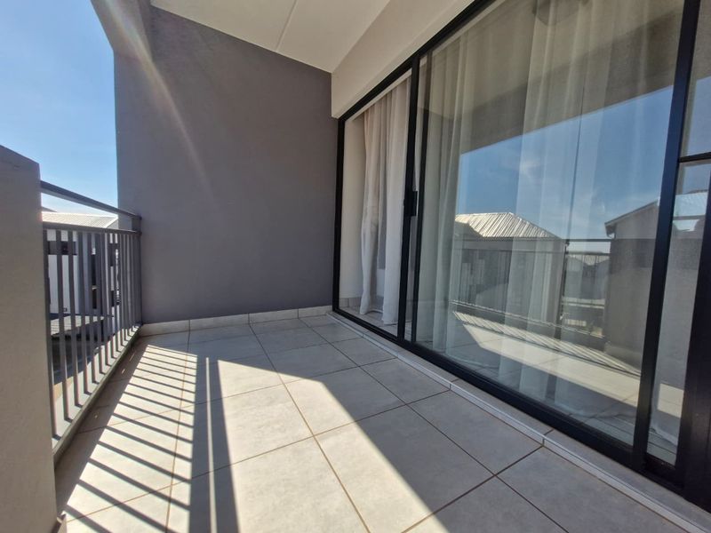 A clean, modern balcony featuring tiled flooring, a metal balustrade, and large sliding glass doors providing access to the interior.