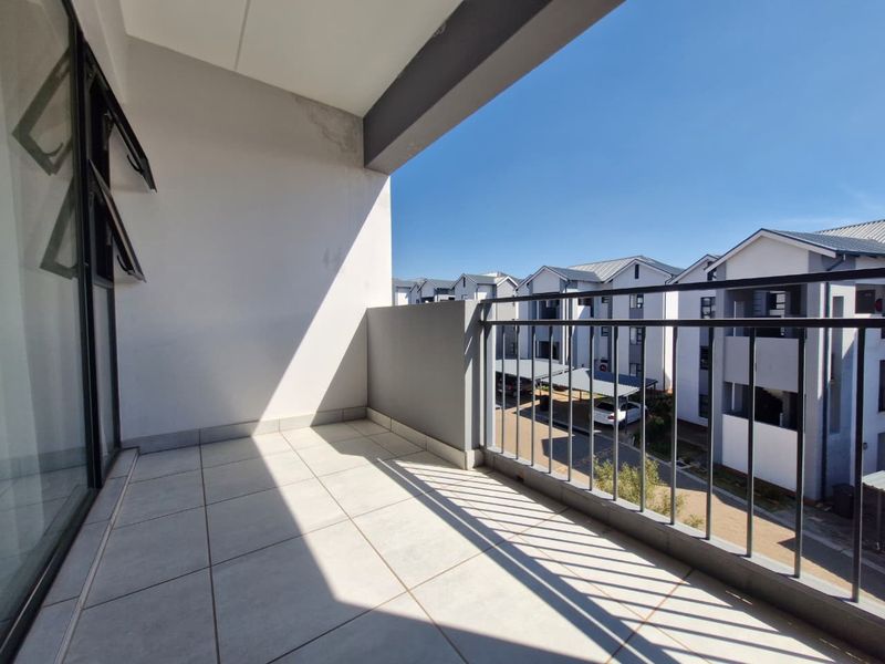 A clean, tiled balcony featuring a metal balustrade and views of the surrounding apartment complex.