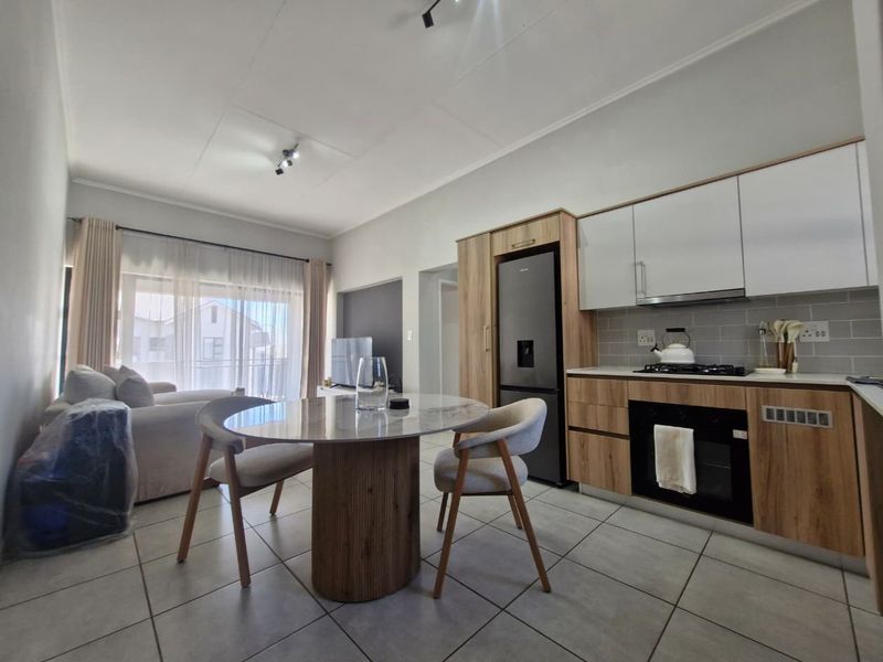Modern open-plan living area featuring a contemporary kitchen with wood-finish cabinetry, gas hob, and tiled flooring, seamlessly flowing into the lounge space.