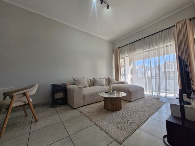 A bright and well-maintained living room featuring neutral tiled flooring and a large sliding glass door that provides access to the balcony.