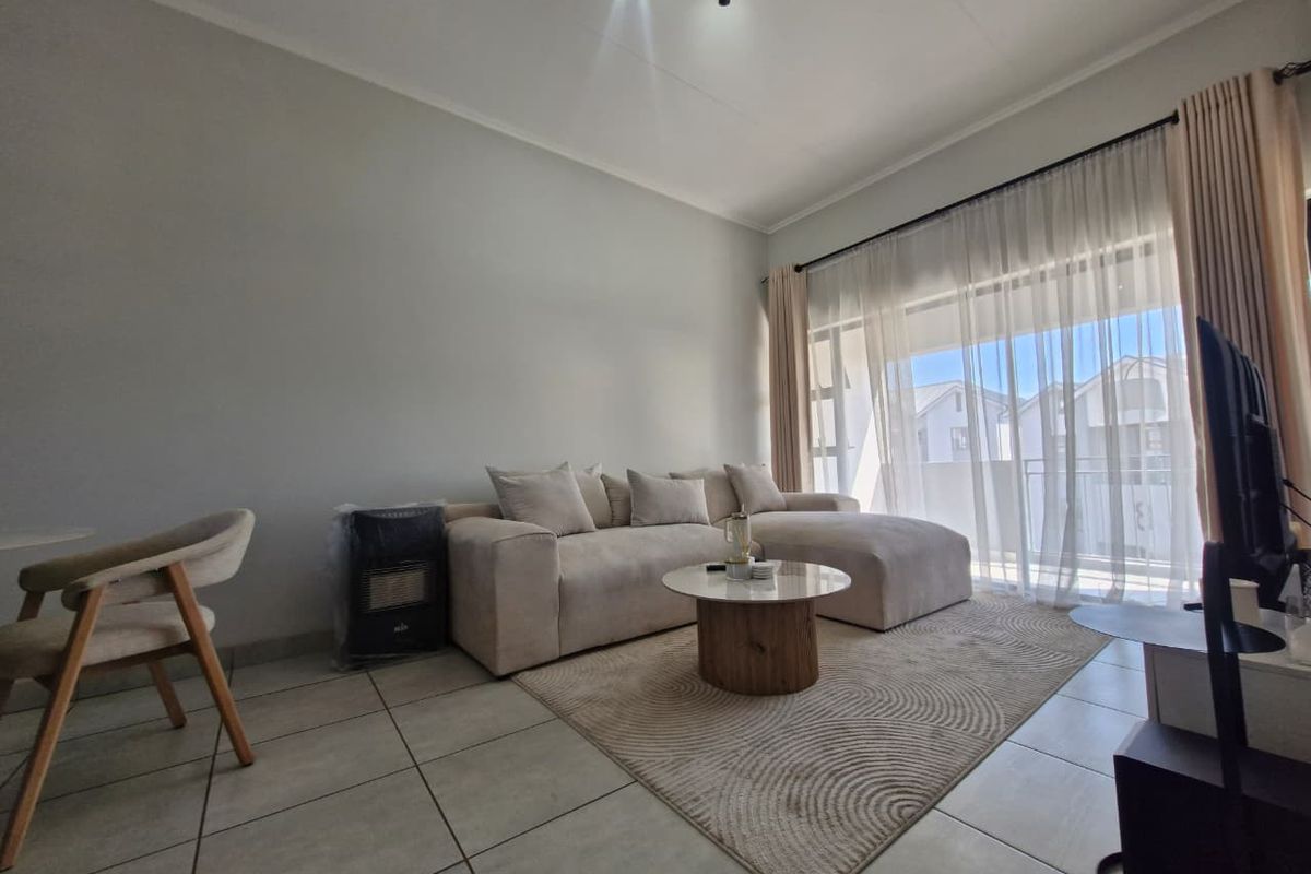 A bright and well-maintained living room featuring neutral tiled flooring and a large sliding glass door that provides access to the balcony.