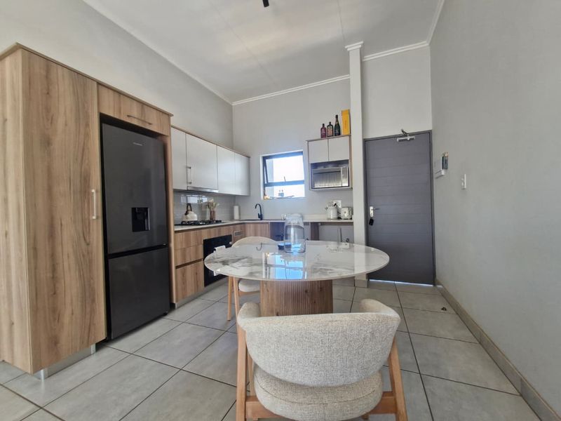 Modern open-plan kitchen featuring wood-finish cabinetry, integrated appliances, and tiled flooring, seamlessly connected to a dining area.