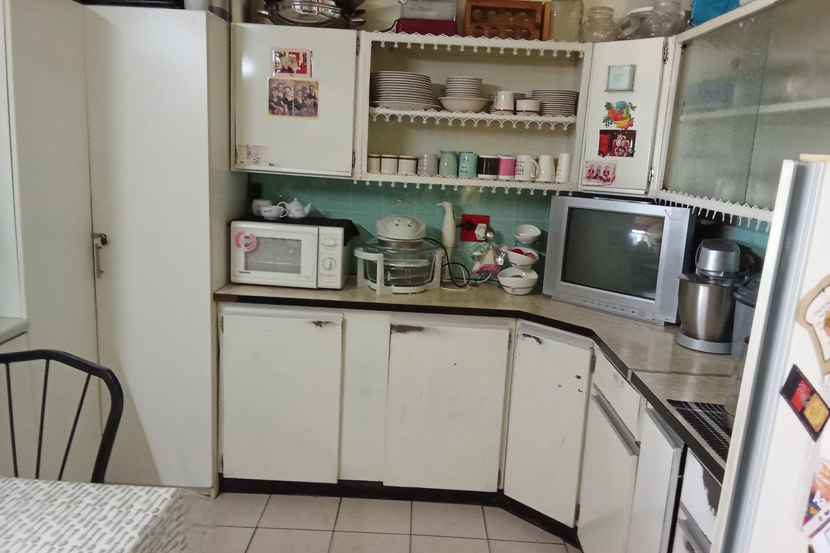 A dated kitchen featuring white built-in cabinetry, laminate countertops, and tiled backsplash, offering potential for a modern renovation.