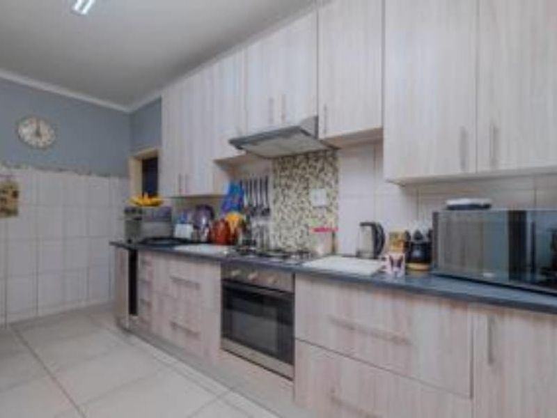 A functional kitchen featuring light wood-finish cabinetry, built-in oven, gas hob, extractor fan, and tiled backsplash with neutral floor tiles.
