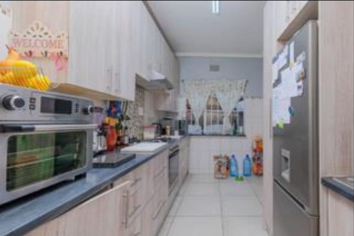 A functional galley-style kitchen featuring light wood-finish cabinetry, laminate countertops, and integrated cooking appliances with tiled flooring.