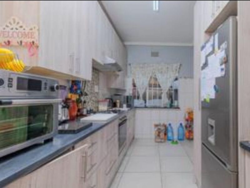 A functional galley-style kitchen featuring light wood-finish cabinetry, laminate countertops, and integrated cooking appliances with tiled flooring.