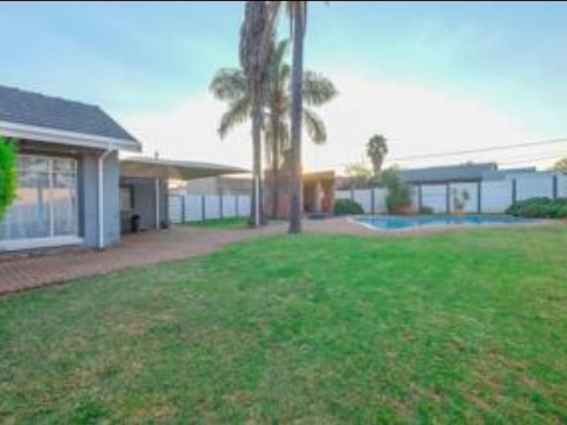 Spacious rear garden featuring a swimming pool, paved patio area, and established lawn, enclosed by boundary walls.
