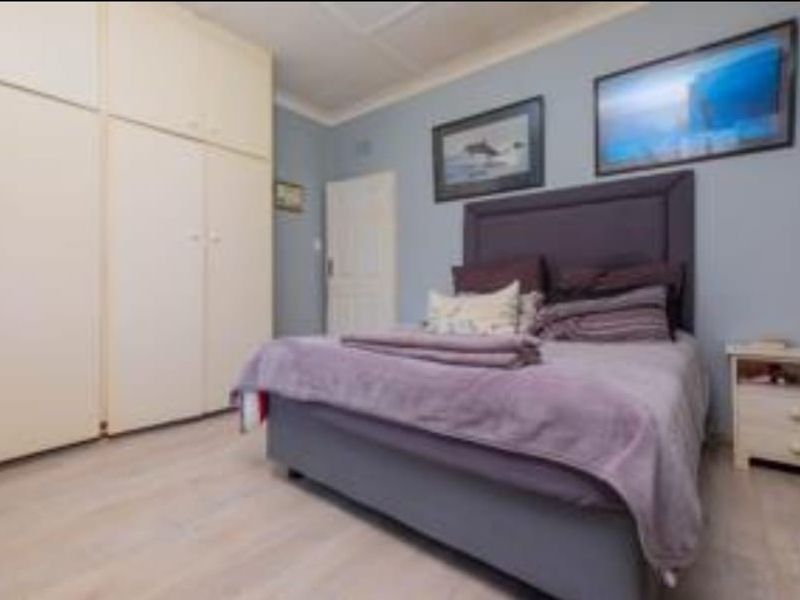 A bedroom featuring light-toned laminate flooring and extensive built-in cupboard storage with a neutral finish.