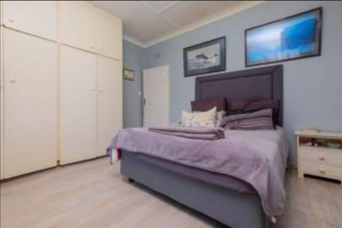 A bedroom featuring light-toned laminate flooring and extensive built-in cupboard storage with a neutral finish.
