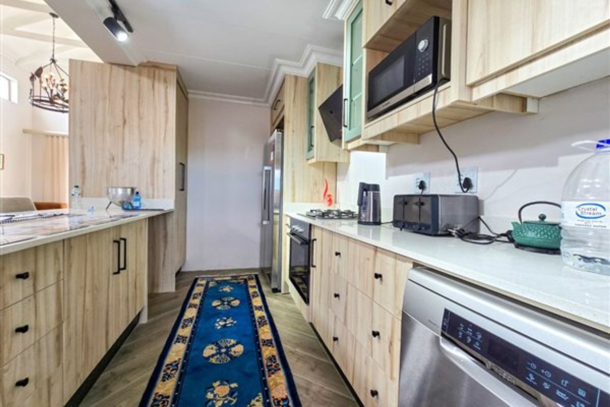 Modern kitchen featuring light wood-grain cabinetry, stone countertops, integrated appliances, and a gas hob, offering a clean and functional culinary space.