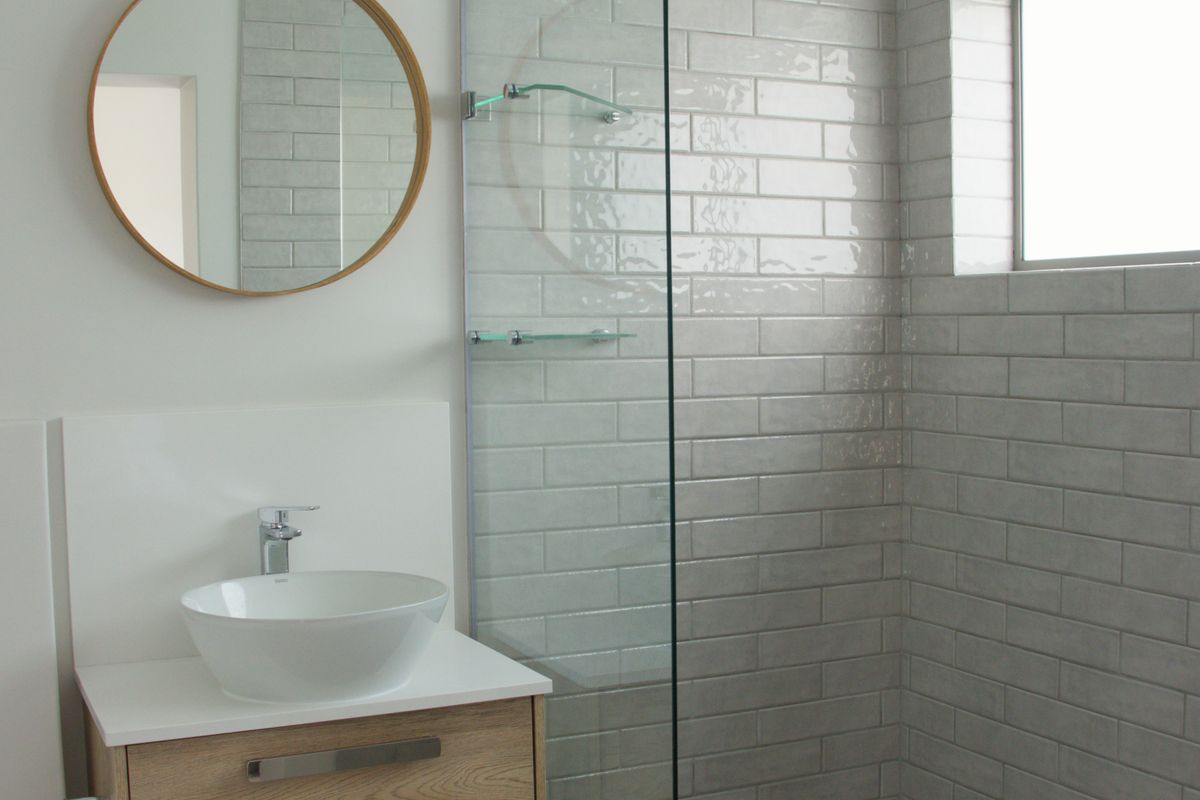 Modern bathroom featuring a wall-mounted wood vanity, vessel sink, and a walk-in shower with grey subway tiles and a glass screen.