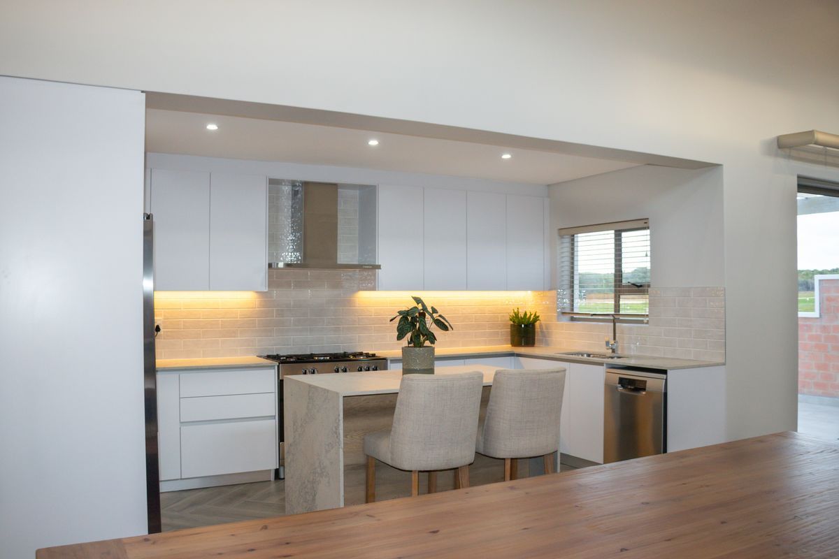 Modern kitchen featuring sleek white cabinetry, stone countertops, subway tile backsplash, integrated appliances, and warm under-cabinet lighting, creating a clean and functional culinary space.