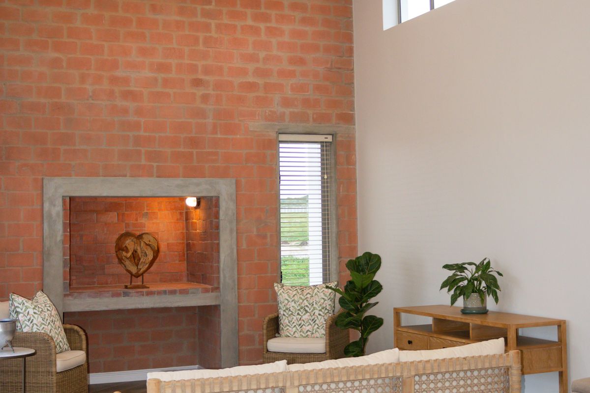 Spacious living room featuring a dramatic vaulted ceiling with exposed trusses, a striking exposed brick wall, built-in fireplace, and modern herringbone tile flooring.