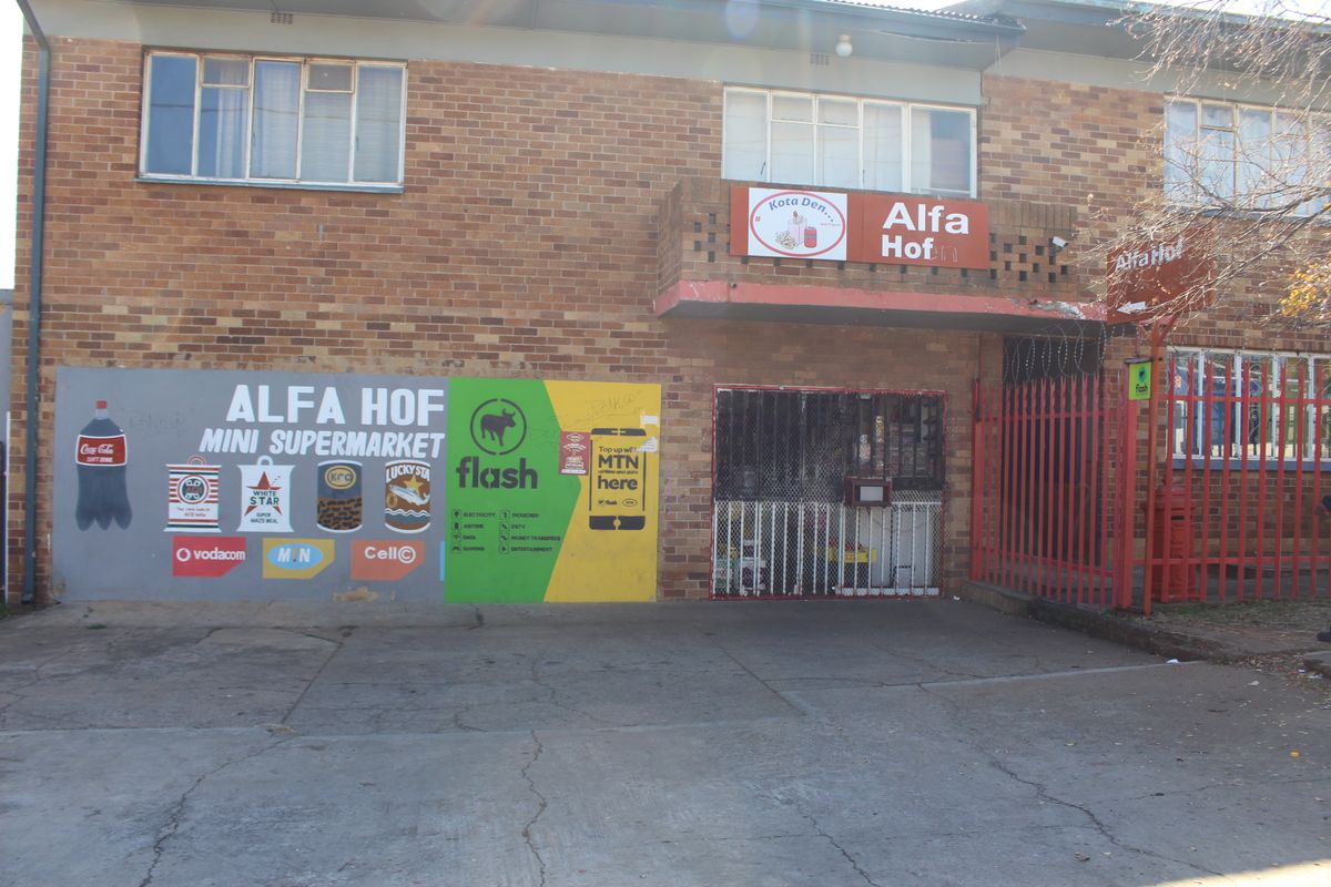 Exterior view of a brick apartment building featuring a ground-floor commercial space with security gate and prominent signage.