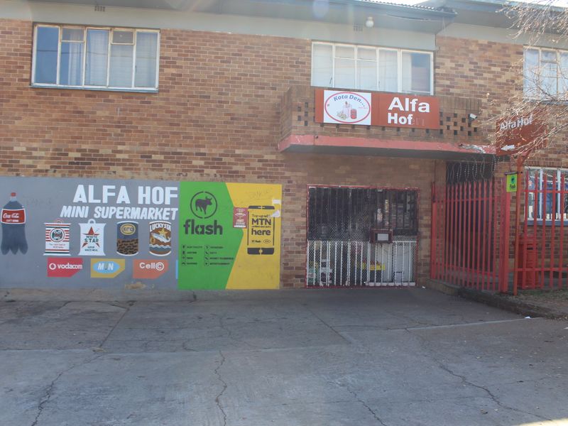 Exterior view of a brick apartment building featuring a ground-floor commercial space with security gate and prominent signage.