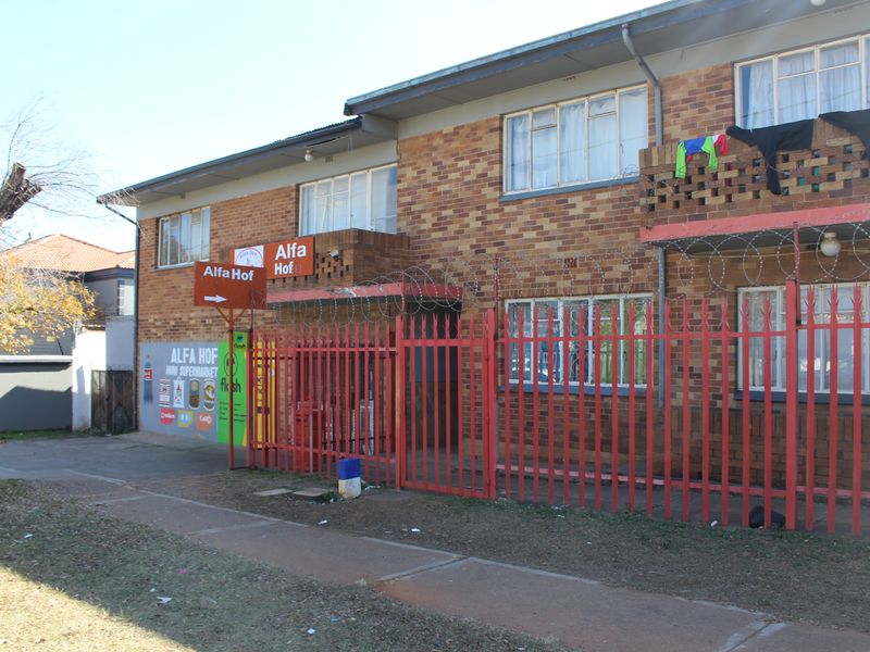 Exterior view of a multi-story brick apartment building featuring security fencing, razor wire, and ground-floor commercial signage.