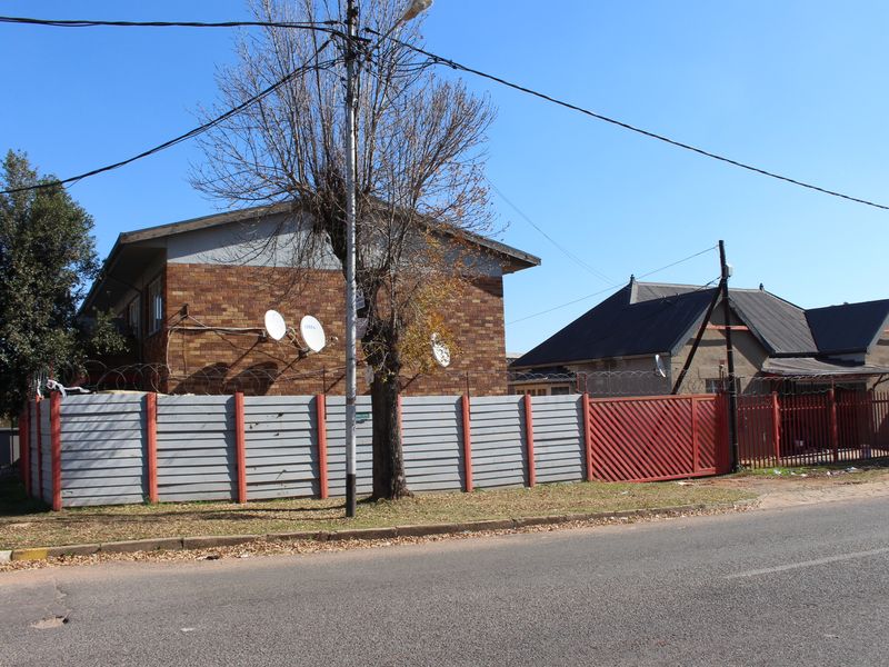 Street view of a brick apartment building featuring perimeter fencing, security razor wire, and satellite dishes.