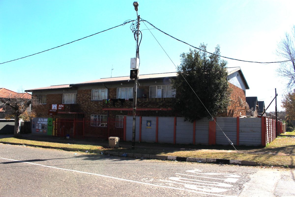 Street view of a multi-story brick apartment building featuring a ground-level retail space and a secure perimeter boundary wall.